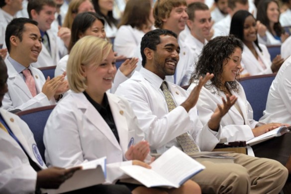 A diverse group of medicals students smiling and clapping in an academic auditorium.