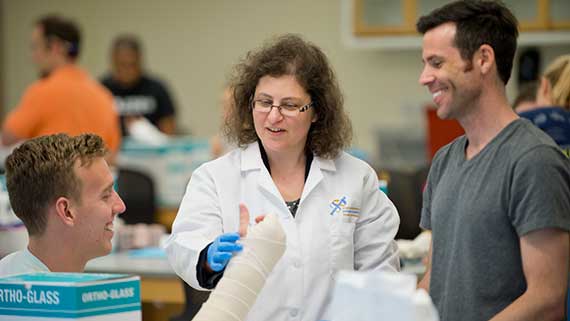 An instructor works with two PA students as they practice splinting.