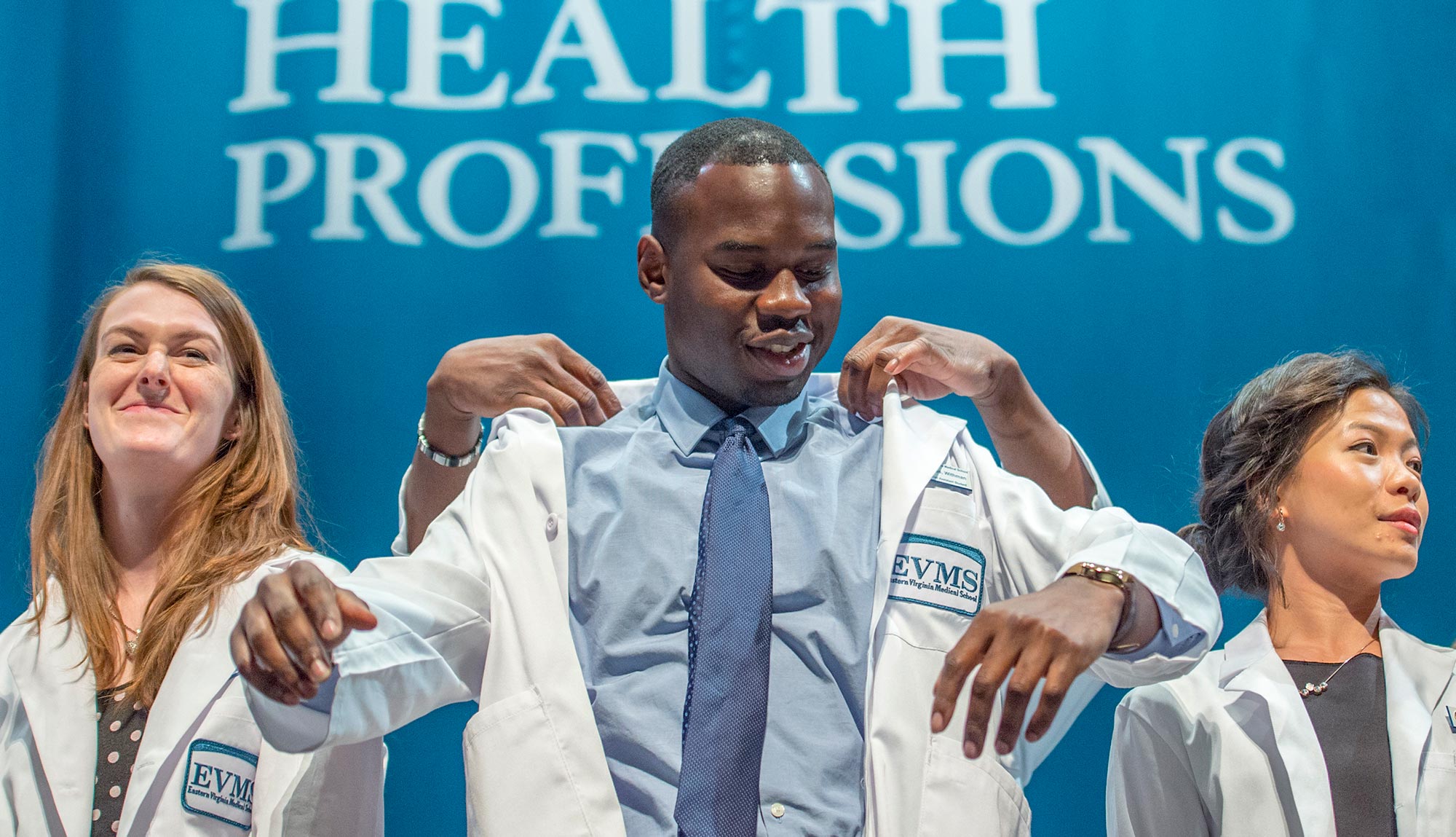 A PA student puts on his white coat during the PA White Coat Ceremony, signifying his transition from student to practitioner.