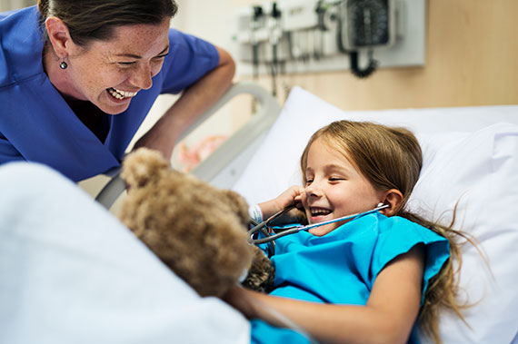 A fellow and patient laugh as the patient uses a stethoscope on her teddy bear.
