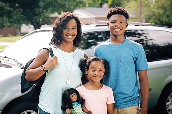 A family poses in front of a vehicle.