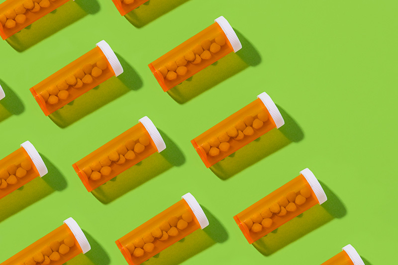 Several bottles of prescription medicine are laying flat against a bright green background.