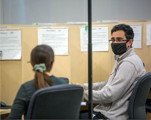 A student sits in a study carrel with a laptop computer. Floor to ceiling windows provide natural light for the space.