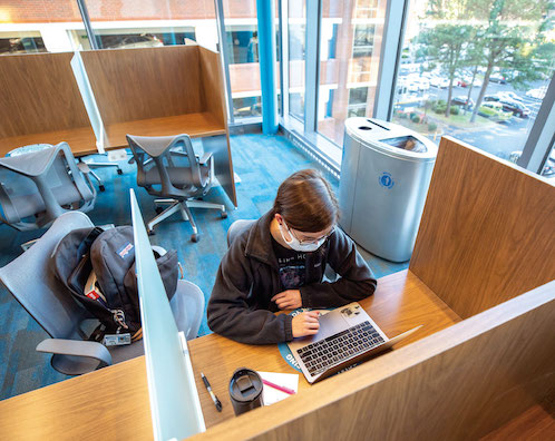 Two students wearing masks talk before the beginning of an exam in the test center in Waitzer Hall. A plastic barrier separates each workstation.