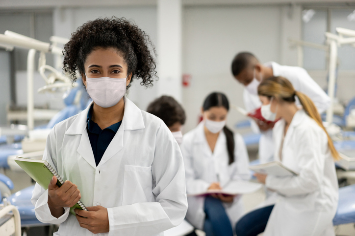 Woman in mask and lab coat in front of a group in lab coats