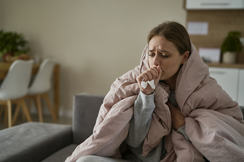 Woman with blanket, tissues and sneezing.