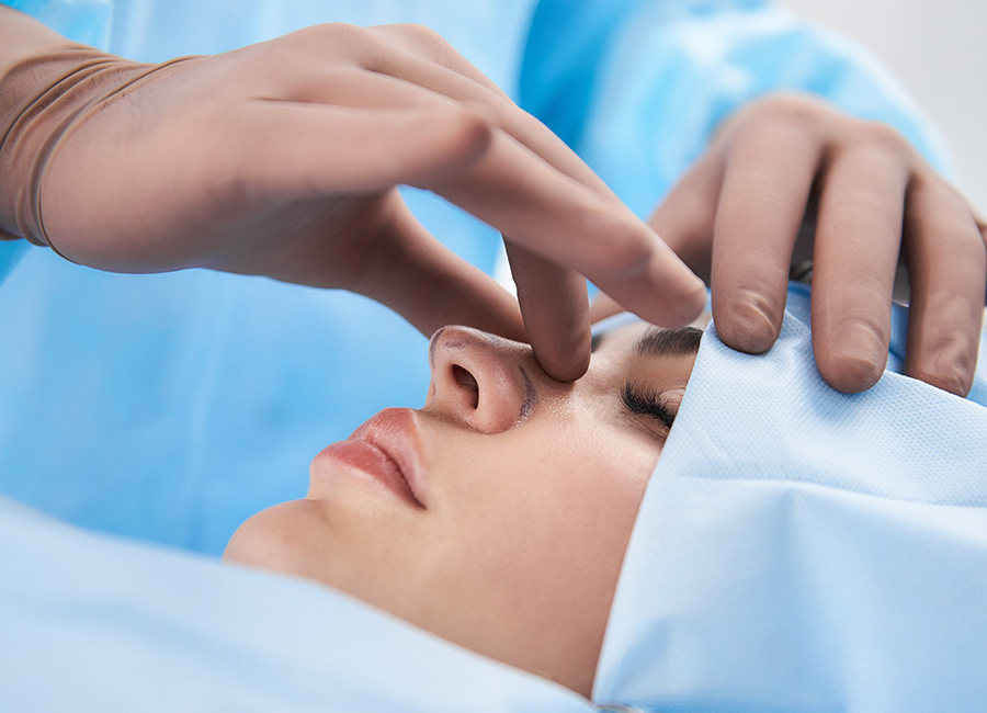 A woman wearing blue scrubs and hair cover is undergoing a rhinoplasty.