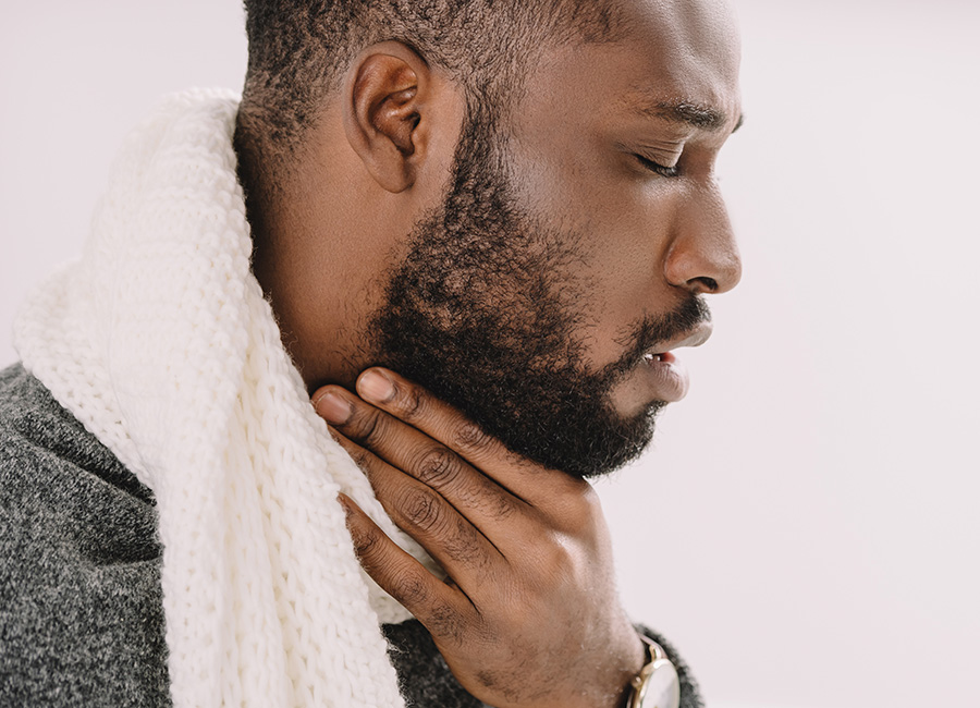 A man wearing a white scarf has a sore throat and is touching his neck.