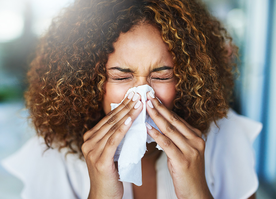 A woman has clogged sinuses and blows her nose using a tissue