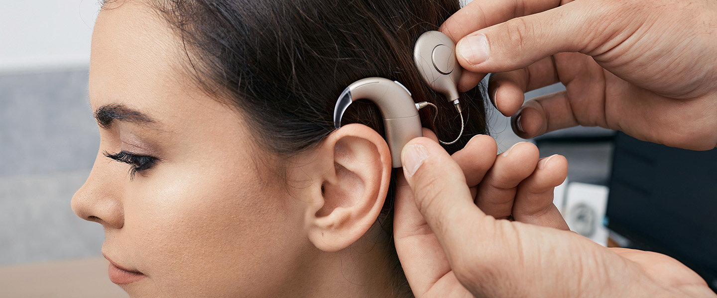 A doctor places a cochlear implant onto a woman's ear and head.
