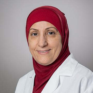 Dr. Sahira Humadi is wearing a red hijab and white medical coat and is smiling at the camera