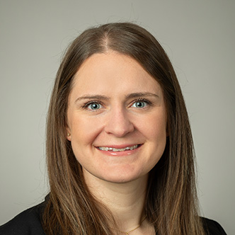 Dr. Lucas has long straight brown hair, is wearing a black blouse, and is smiling at the camera.