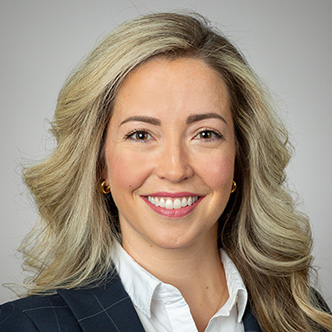 Dr. Palin has long wavy blonde hair, is wearing a dark blazer with a white shirt underneath, and is smiling at the camera.