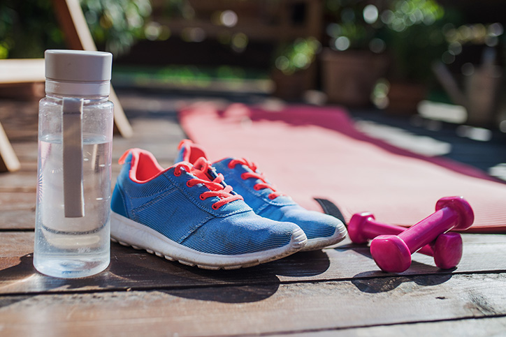 Close up of clear sports water bottle, blue sneakers with orange laces, and pink hand weights
