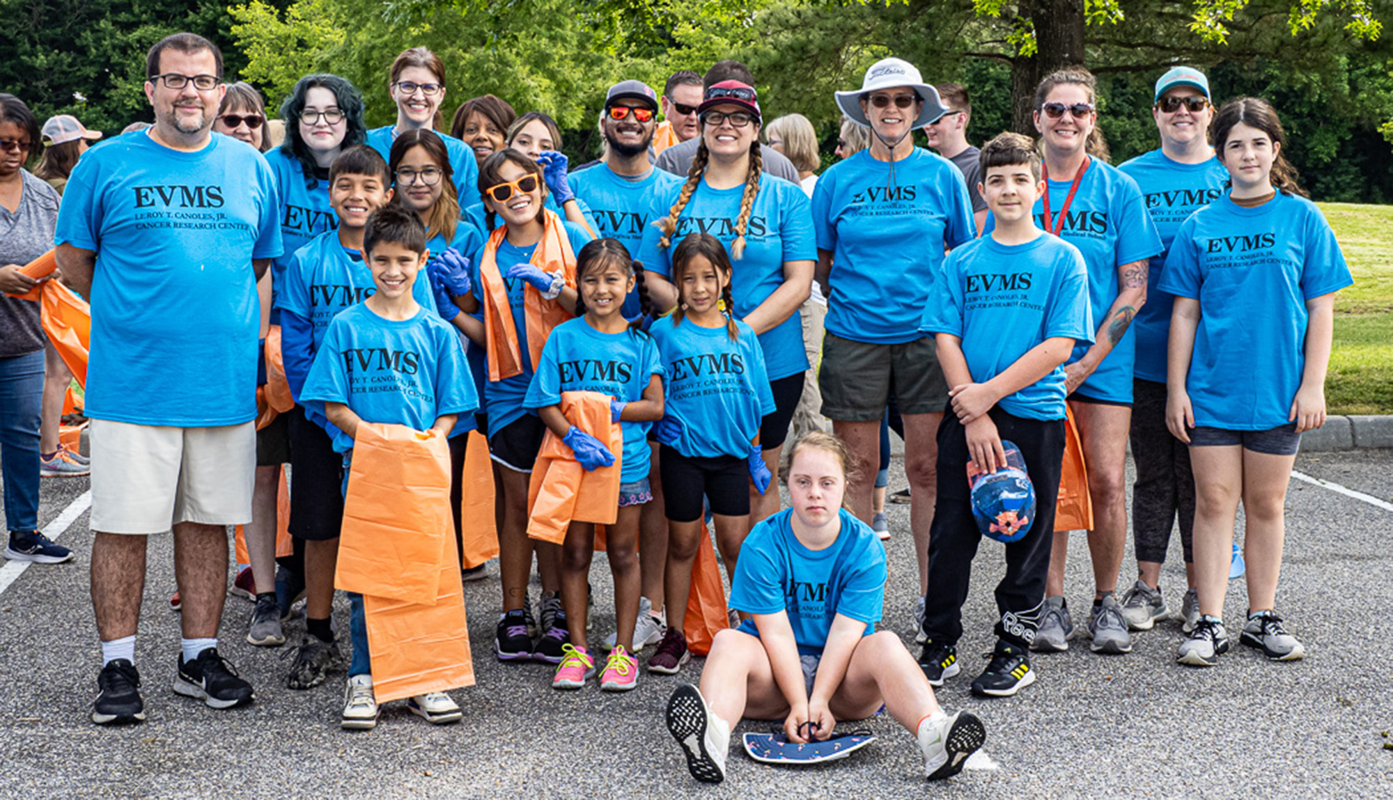 A group of people wearing blue t-shirts pose for photo while holding orange trash bags and other gear to collect trash.