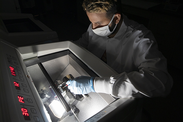 Male in gloves and mask working at a large piece of lab equipment with a digital readout