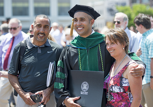 A hooded male graduate poses for photos with a male and female family member.