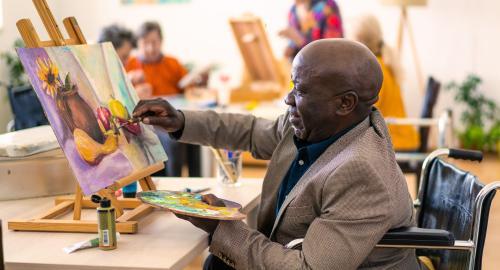 Black man in wheelchair painting a canvas
