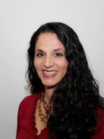 A woman with long dark hair wearing a red blouse smiles at the camera