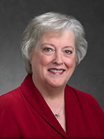A woman with short gray hair wearing a red blouse smiles at the camera