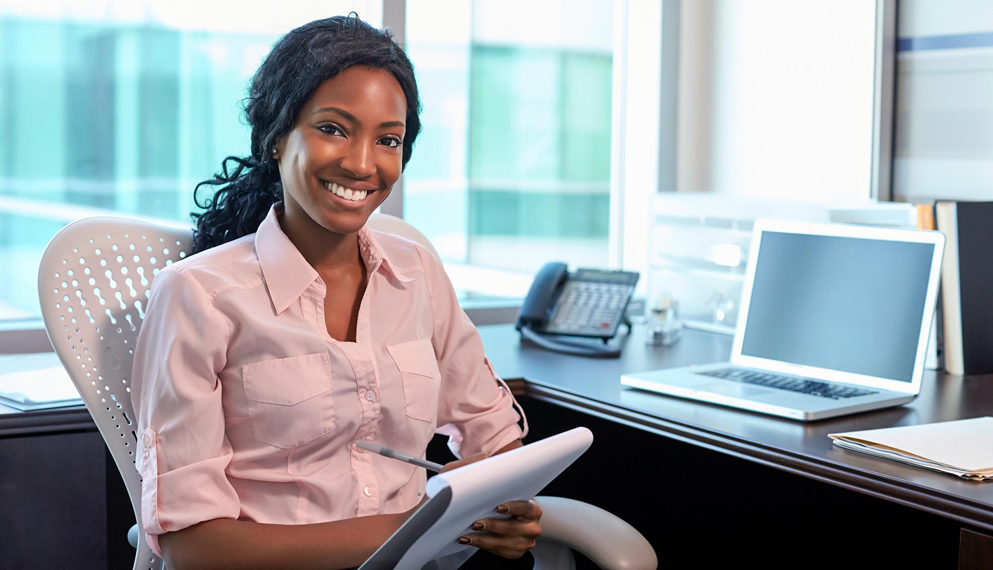 An educator sits in front of a computer with a note pad. 