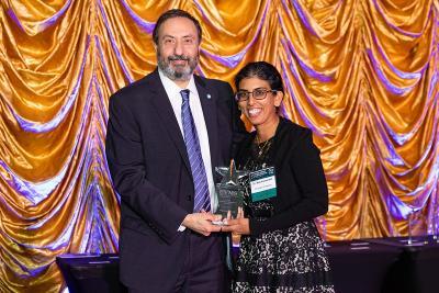 A photo of Dr. Alfred Abuhamad and Dr. Mily Kannarkat holding a trophy. Dr. Abuhamad is presenting Dr. Kannarkat with the award in honor of her winning the Fine Family Academy Of Educators Awards FFAOE Award for Educational Leadership for 2023.
