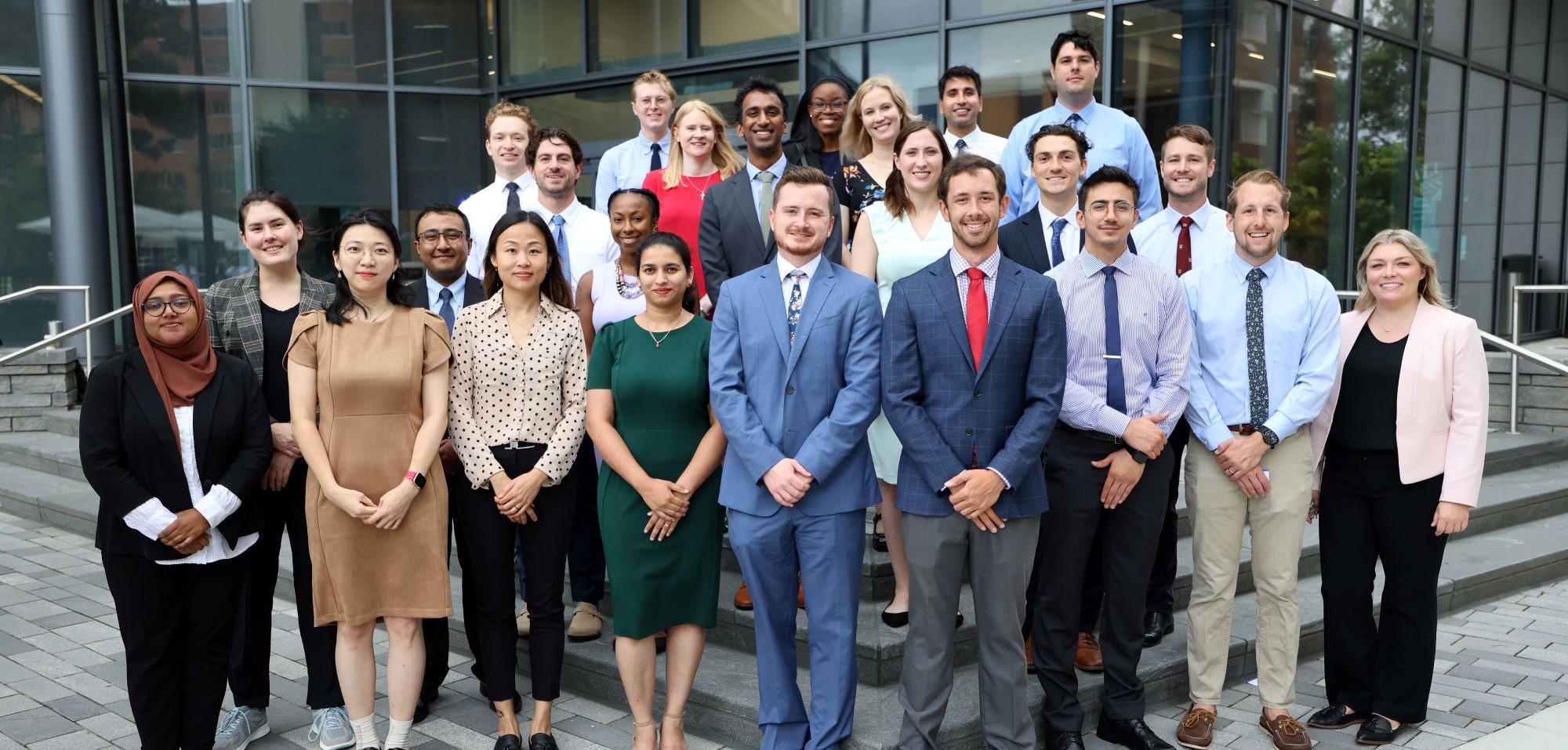 A group of new resident physicians for the EVMS Internal Medicine Residency Program wearing business casual clothing and smiling for the camera on the steps of Waitzer Hall.