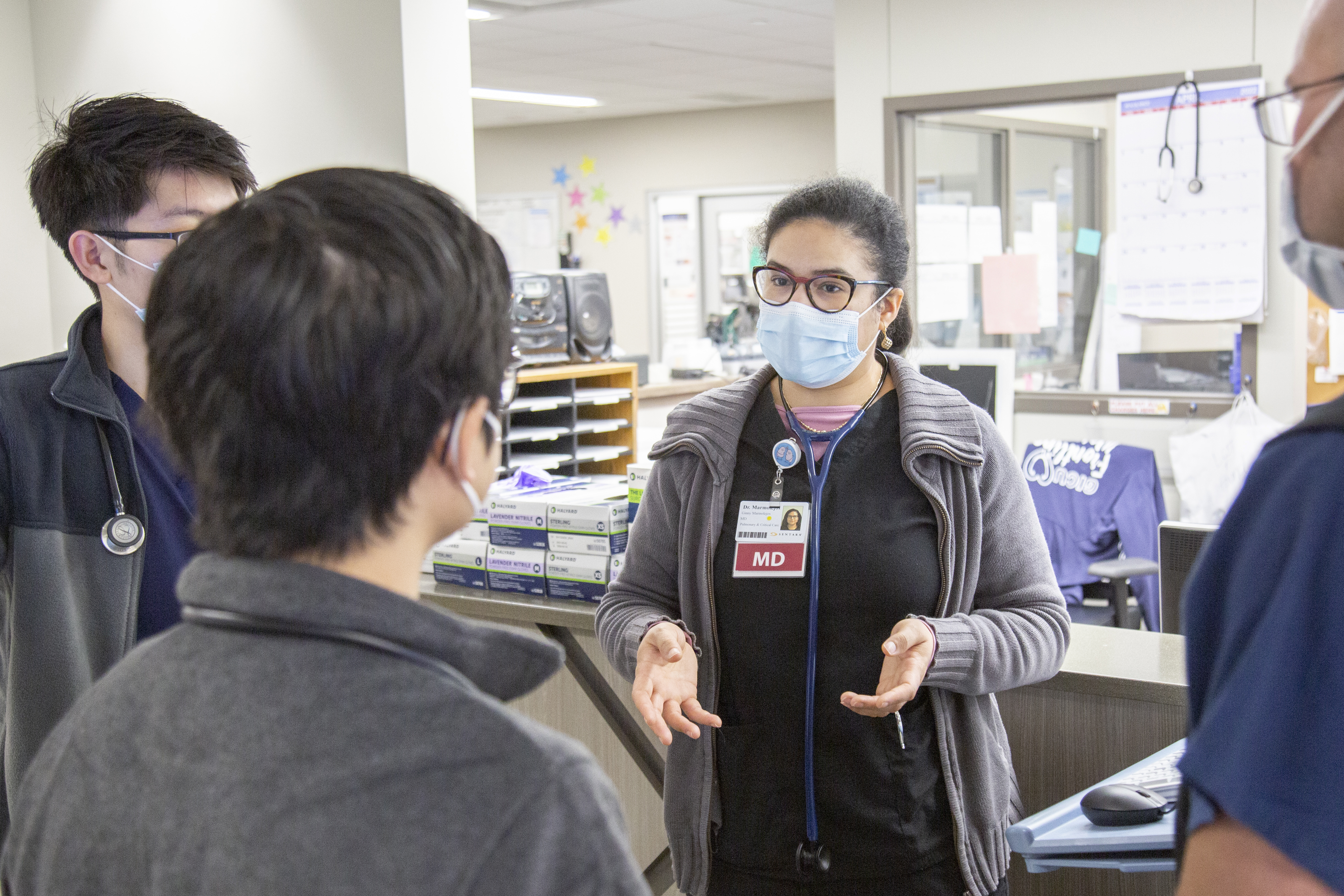 A female doctor explaining something to 3 other health care professionals with a mask.