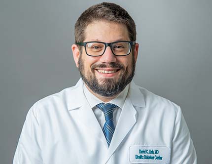 David Lieb, MD, FACE, FACP, smiles at the camera wearing his white coat and glasses.