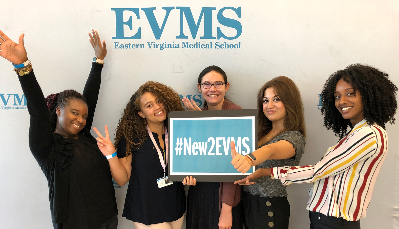 Five young women holding a sign with social media hashtag NewToEVMS