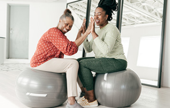 two women high five-ing on pilates balls.