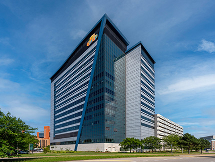 Looking up at a tall building with blue accents and mirrored windows surrounded by trees