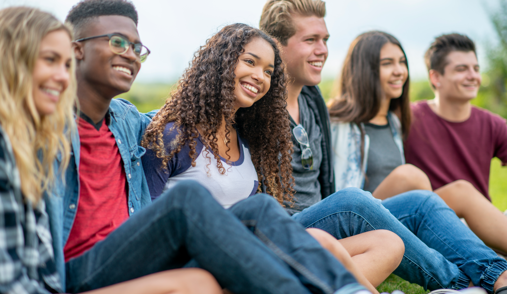 A small group of teenagers sit in the grass as they hang out talking and enjoying a few laughs together.
