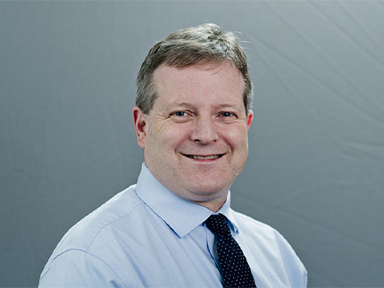 Dr. Richard W. Handel smiling for a professional headshot, wearing a blue dress shirt and a navy-blue tie with white polka dots.