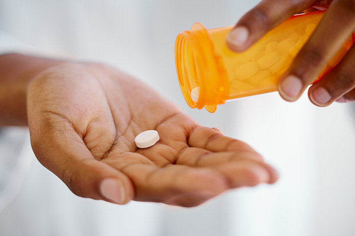 Close-up of one person's two hands, one holding a prescription bottle and one holding a white pill