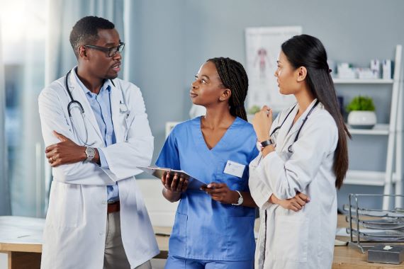 Three doctors and a woman in blue scrubs discuss a report
