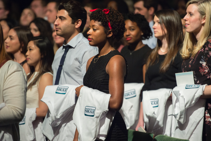A crowd of EVMS students hold white coats during a ceremony