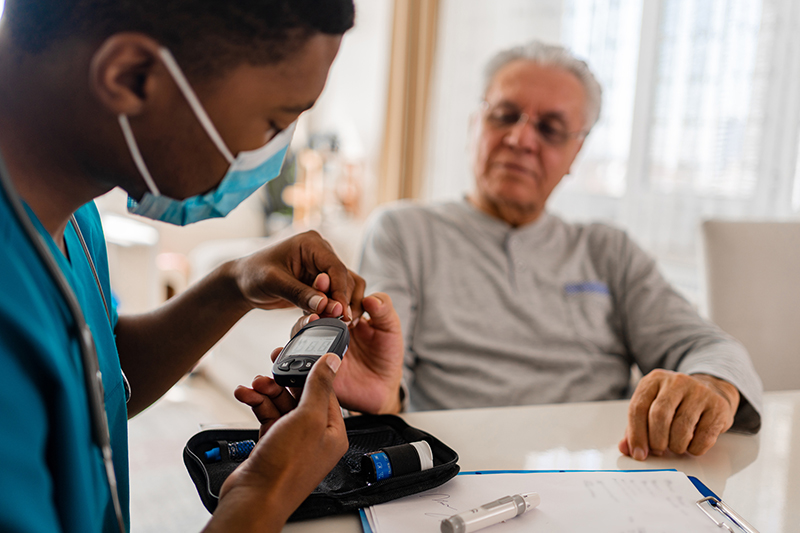 A healthcare professional wearing a mask takes a sample of an older patient's blood to test for blood sugar.