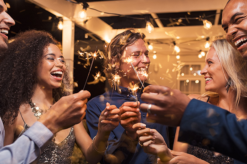 Five friends laugh and smile at a party while holding sparkers