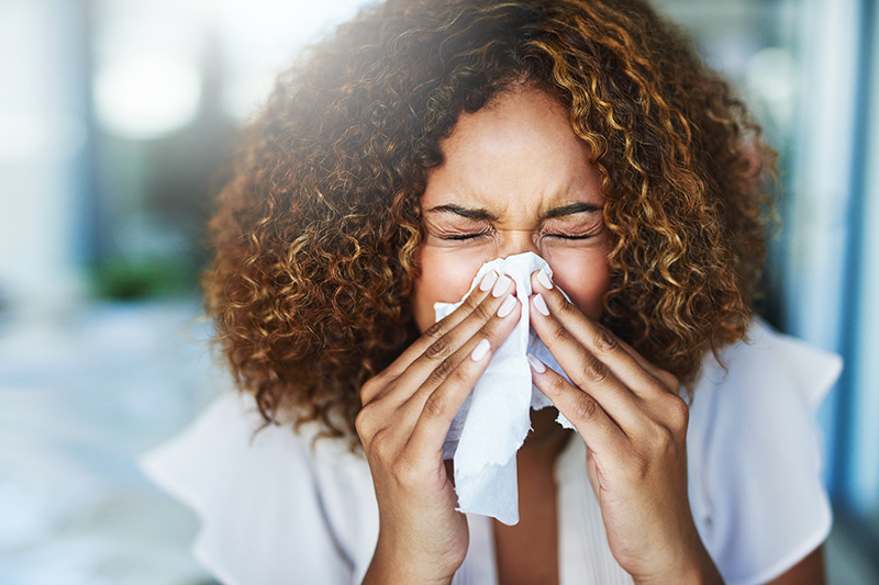 A woman with brown curly hair sneezes into a tissue.