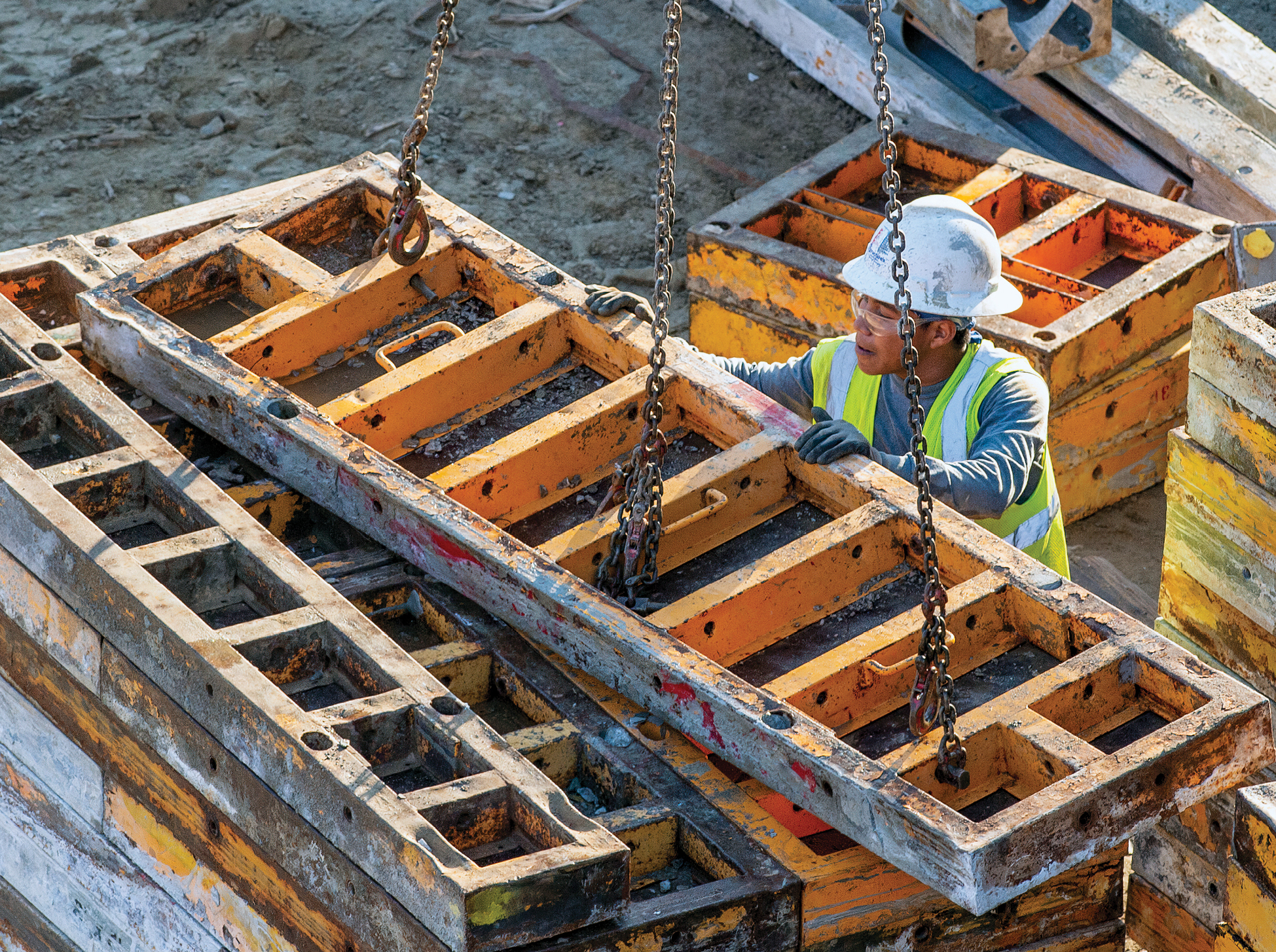 A worker stacks concrete forms lowered from a crane.