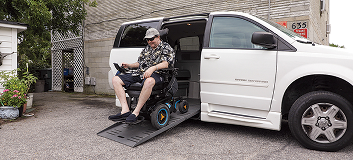 Eddie using his wheel chair to exit off of a ramp from the side of his specially equipped van.