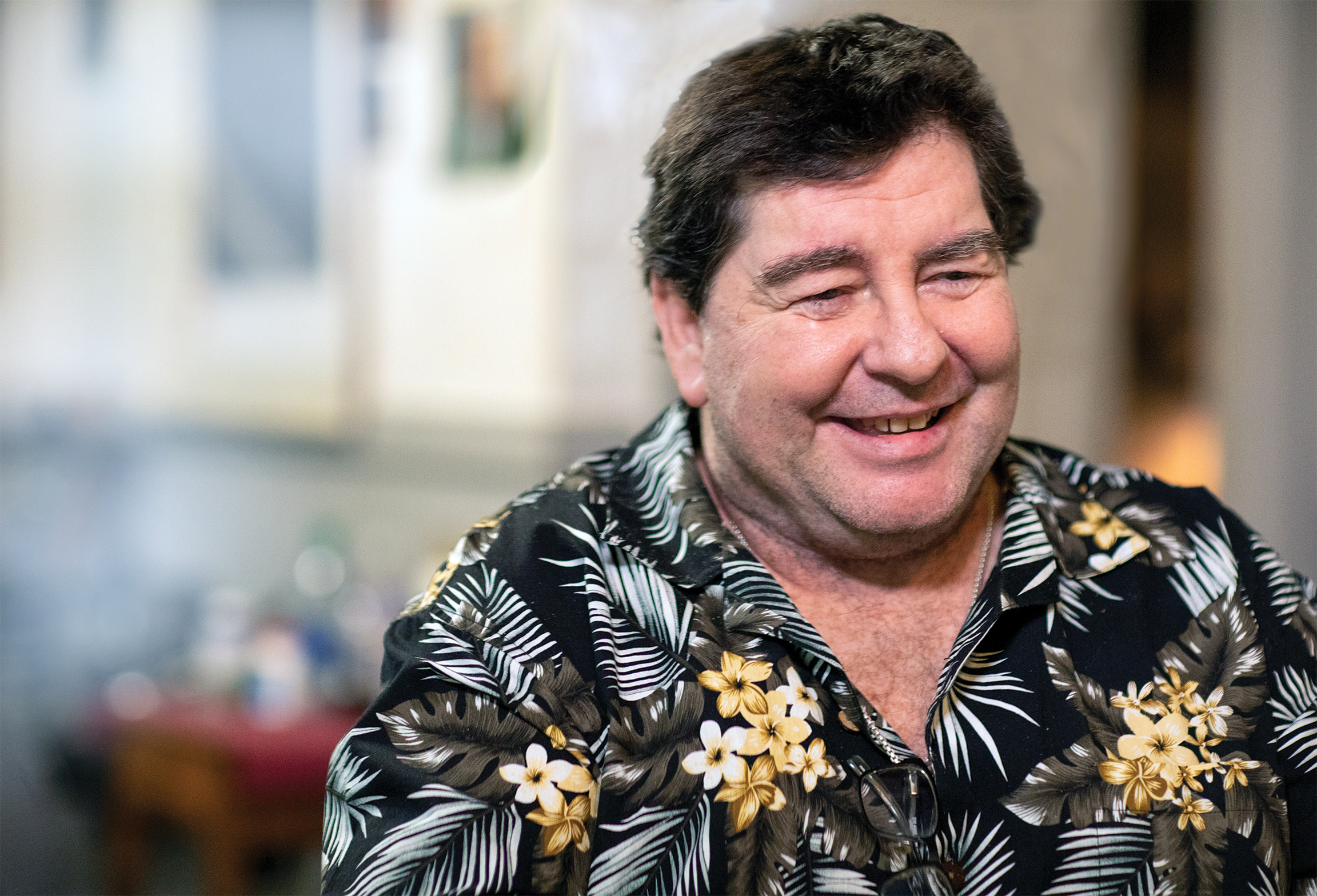 A smiling Eddie Roebuck wearing a tropical print shirt looks away from the camera.