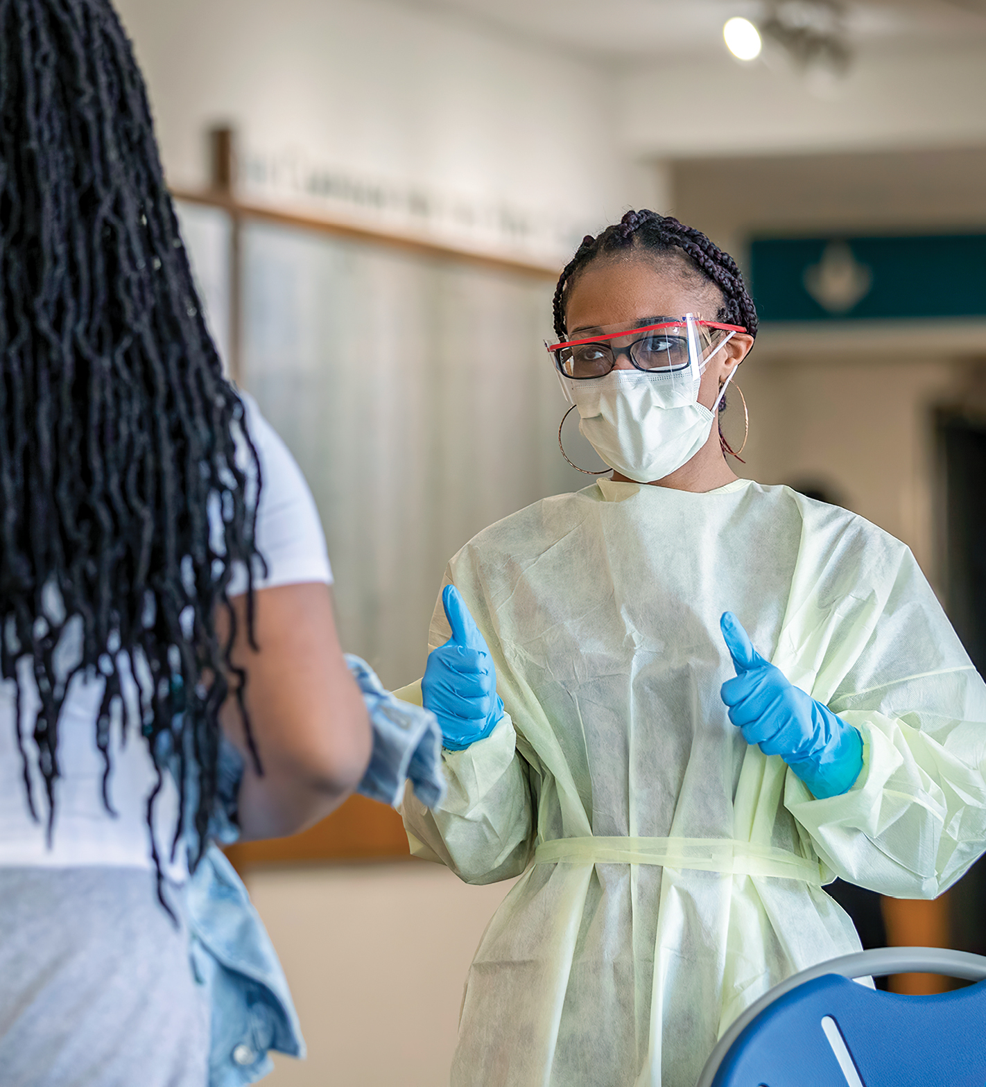 Nikia Holley at Hofheimer Hall giving a thumbs up to a patient after screening the patient for COVID-19 symptoms. She is wearing a face mask, a partial face shield, medical gloves and a medical gown.