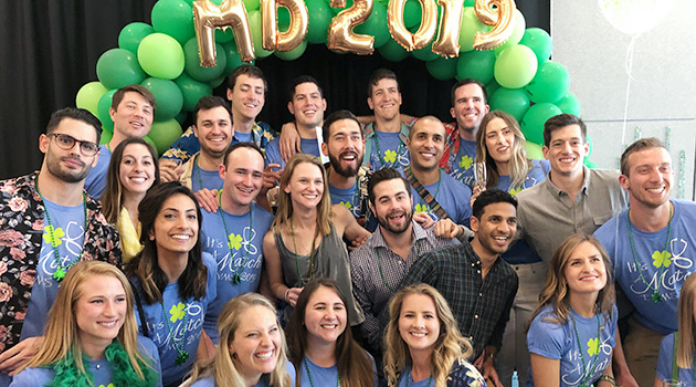 Group of fourth-year EVMS medical students posing with balloons in the background.