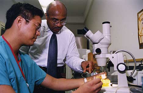 A colorized image of Dr. Britt assisting a student with using a microscope